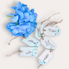 Load image into Gallery viewer, Calming Creek Sachets by Pure Essence Scent-white scented wax decorated with dried botanicals and pebbles for decoration, and twine loop for hanging.