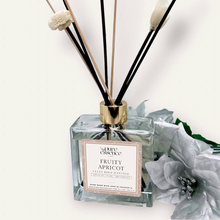 Load image into Gallery viewer, Fruity Apricot Reed Diffuser by Pure Essence Scent-A glass reed diffuser filled with scented liquid. There’s a gold cap and black/natural reeds, some featuring decorative flowers.