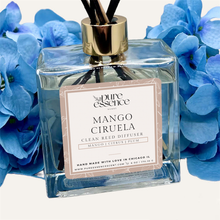 Load image into Gallery viewer, Mango Ciruela Reed Diffuser by Pure Essence Scent-A glass reed diffuser filled with scented liquid. There’s a gold cap and black/natural reeds, some featuring decorative flowers.