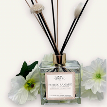 Load image into Gallery viewer, Pomegranade Reed Diffuser by Pure Essence Scent-A glass reed diffuser filled with scented liquid. There’s a gold cap and black/natural reeds, some featuring decorative flowers.