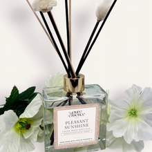 Load image into Gallery viewer, Pleasant Sunshine Reed Diffuser by Pure Essence Scent-A glass reed diffuser filled with scented liquid. There’s a gold cap and black/natural reeds, some featuring decorative flowers.