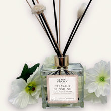 Load image into Gallery viewer, Pleasant Sunshine Reed Diffuser by Pure Essence Scent-A glass reed diffuser filled with scented liquid. There’s a gold cap and black/natural reeds, some featuring decorative flowers.