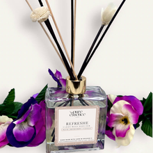 Load image into Gallery viewer, Refreshe Reed Diffuser by Pure Essence Scent-A glass reed diffuser filled with scented liquid. There’s a gold cap and black/natural reeds, some featuring decorative flowers.
