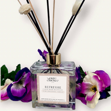 Load image into Gallery viewer, Refreshe Reed Diffuser by Pure Essence Scent-A glass reed diffuser filled with scented liquid. There’s a gold cap and black/natural reeds, some featuring decorative flowers.